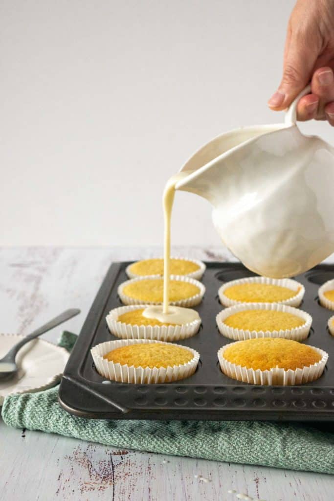 Pouring the tres leches mix on cupcakes on a muffin tin