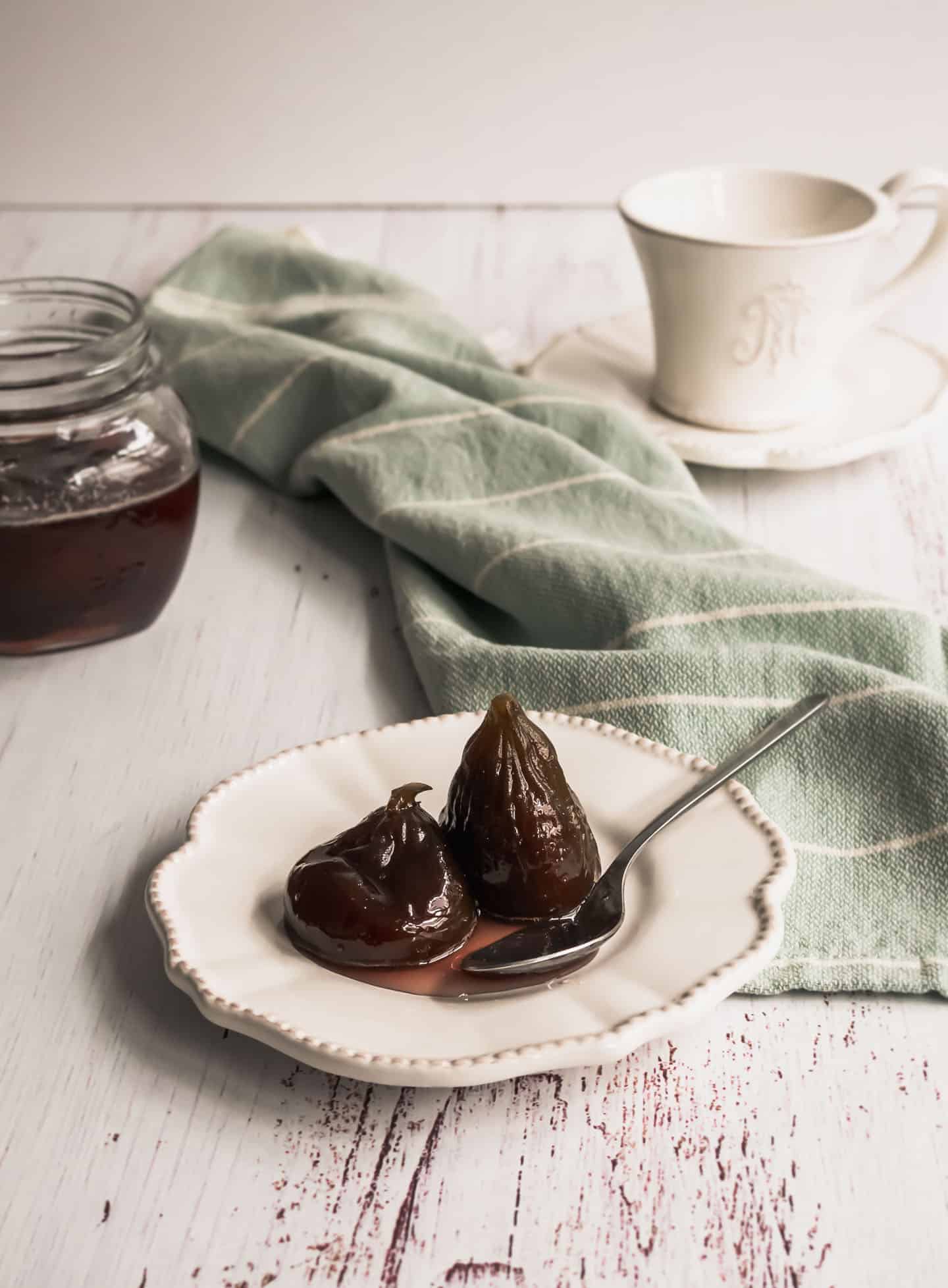 Figs in Syrup in front of a open jar with figs and a tea cup