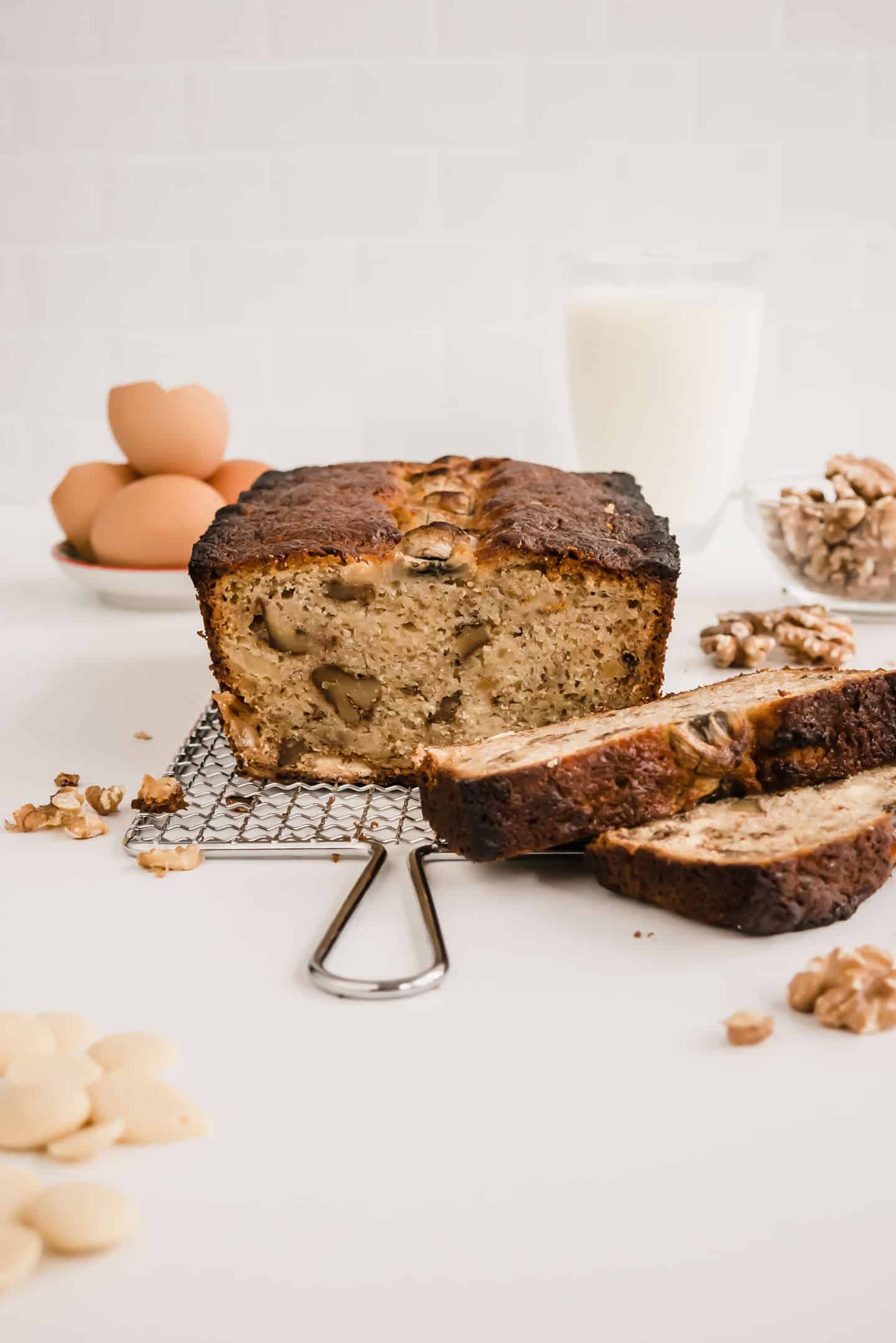 Banana bread and some slices with a glass of milk and some eggs shells at the back