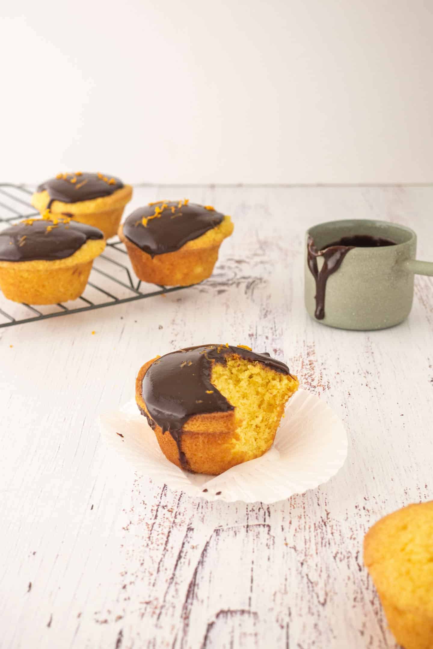 Mandarin Muffins on a cooling rack, another one already bitten and a little jar with some chocolate ganache dripping.