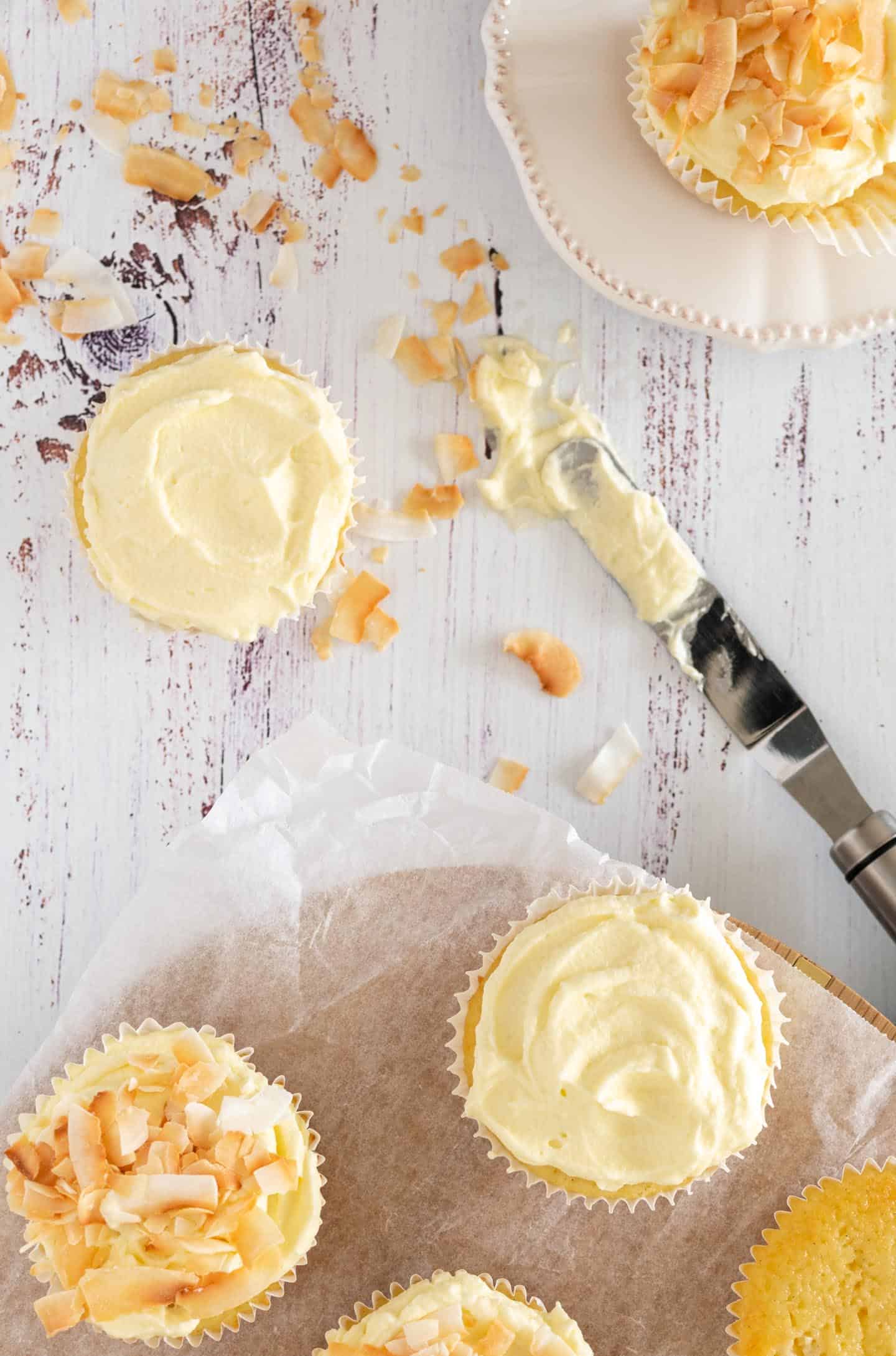 Preparación de cupcakes Tres Leches de coco, una espátula pequeña, algunos cupcakes solo con crema batida por encima, otros sobre una base de madera.