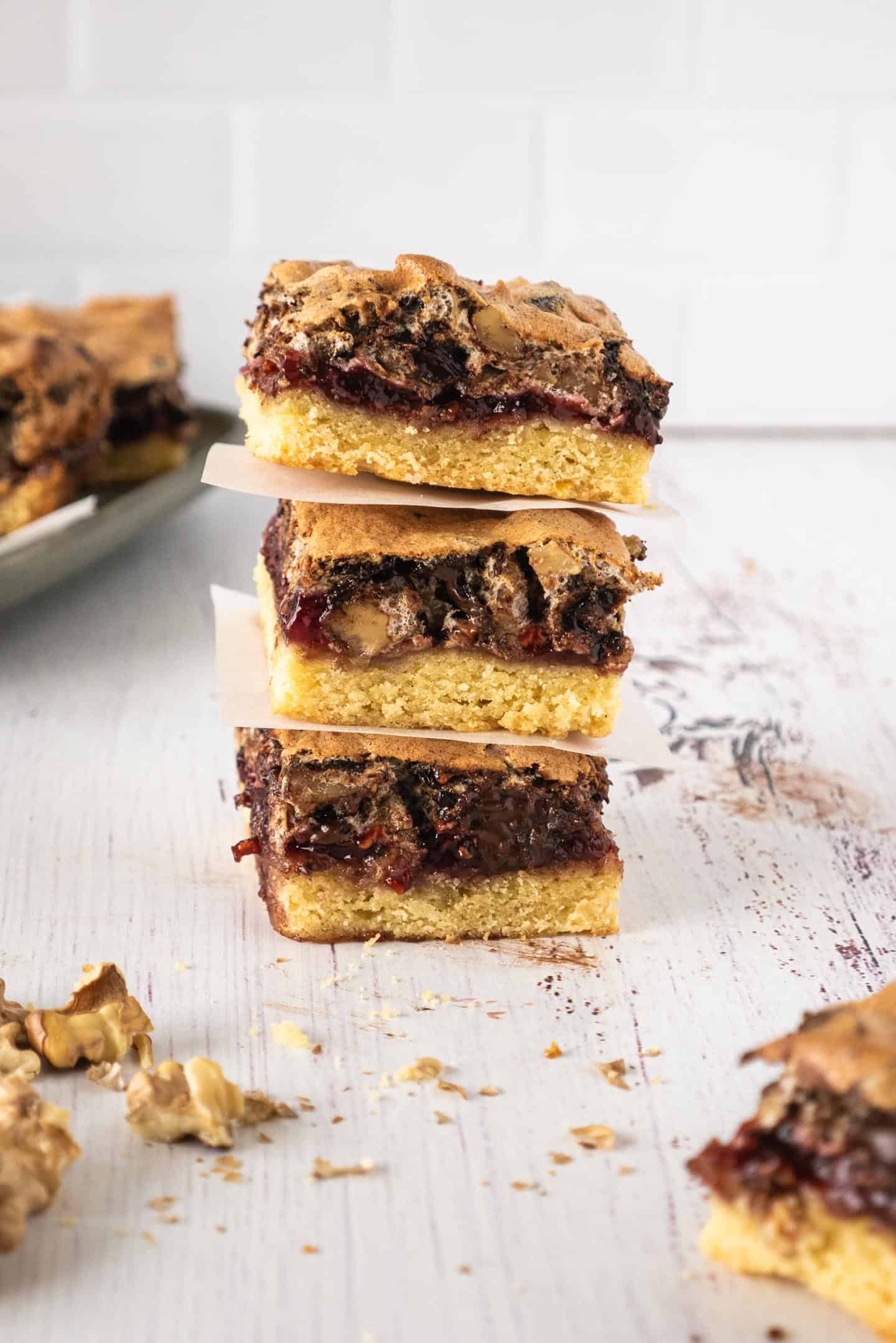 Three square raspberry bars with chocolate and walnuts meringue, and a plate with more tart at the back