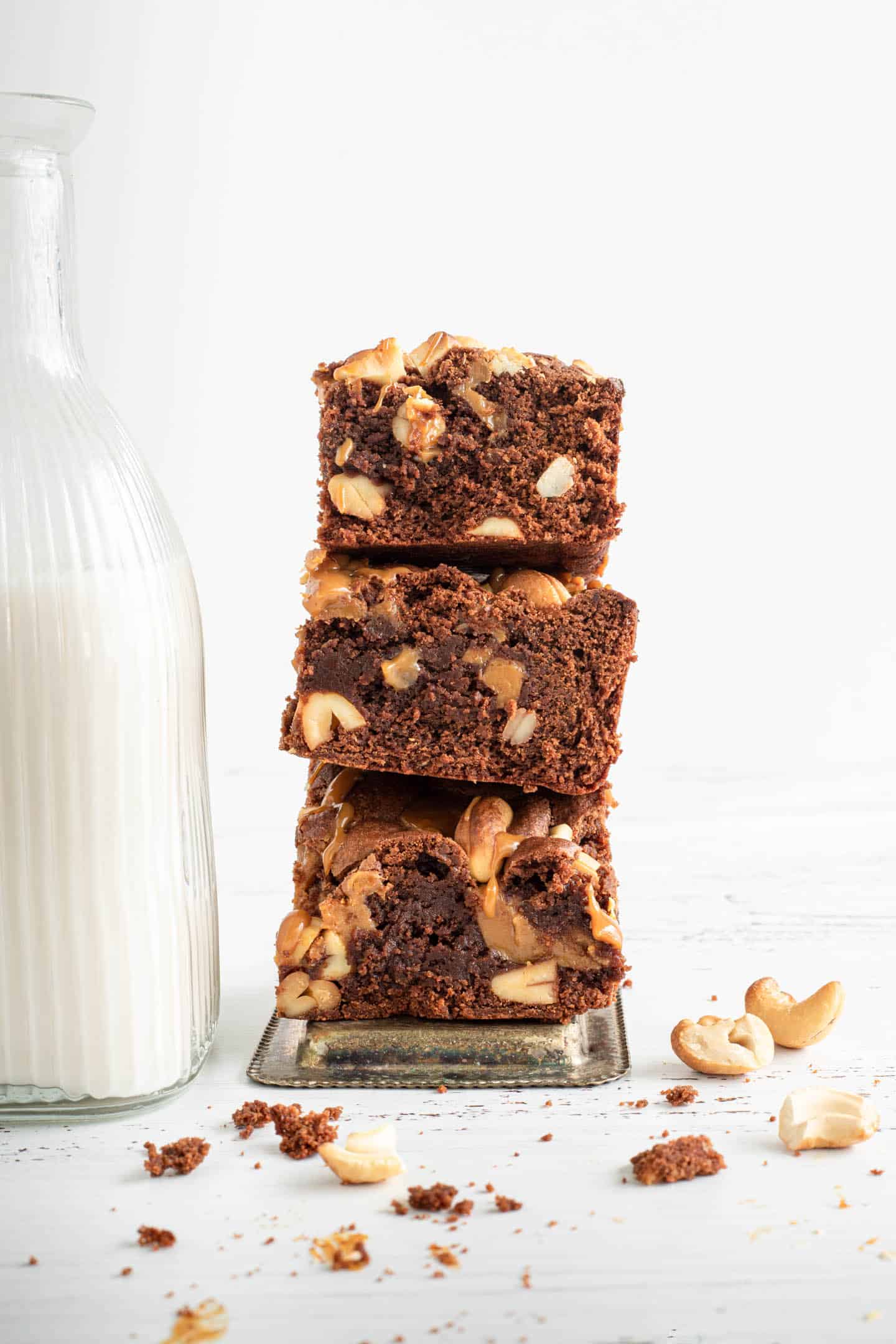 Three squares of dulce de leche brownies piled on the side of a bottle of milk and cashews around