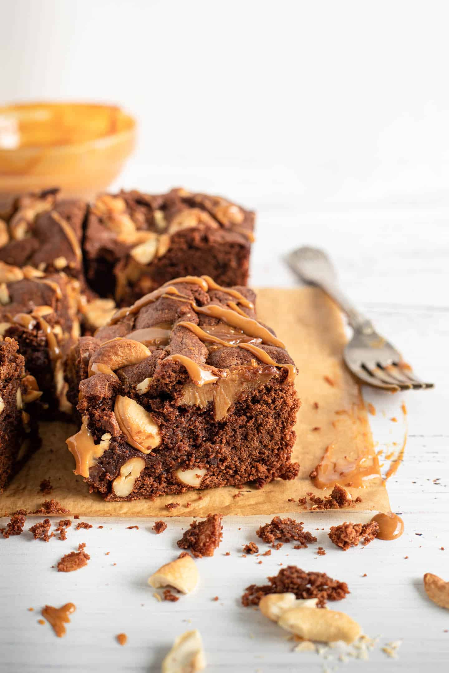 Brownies with cashews and dulce de leche cut into squares on brown parchment paper, and a fork on the side