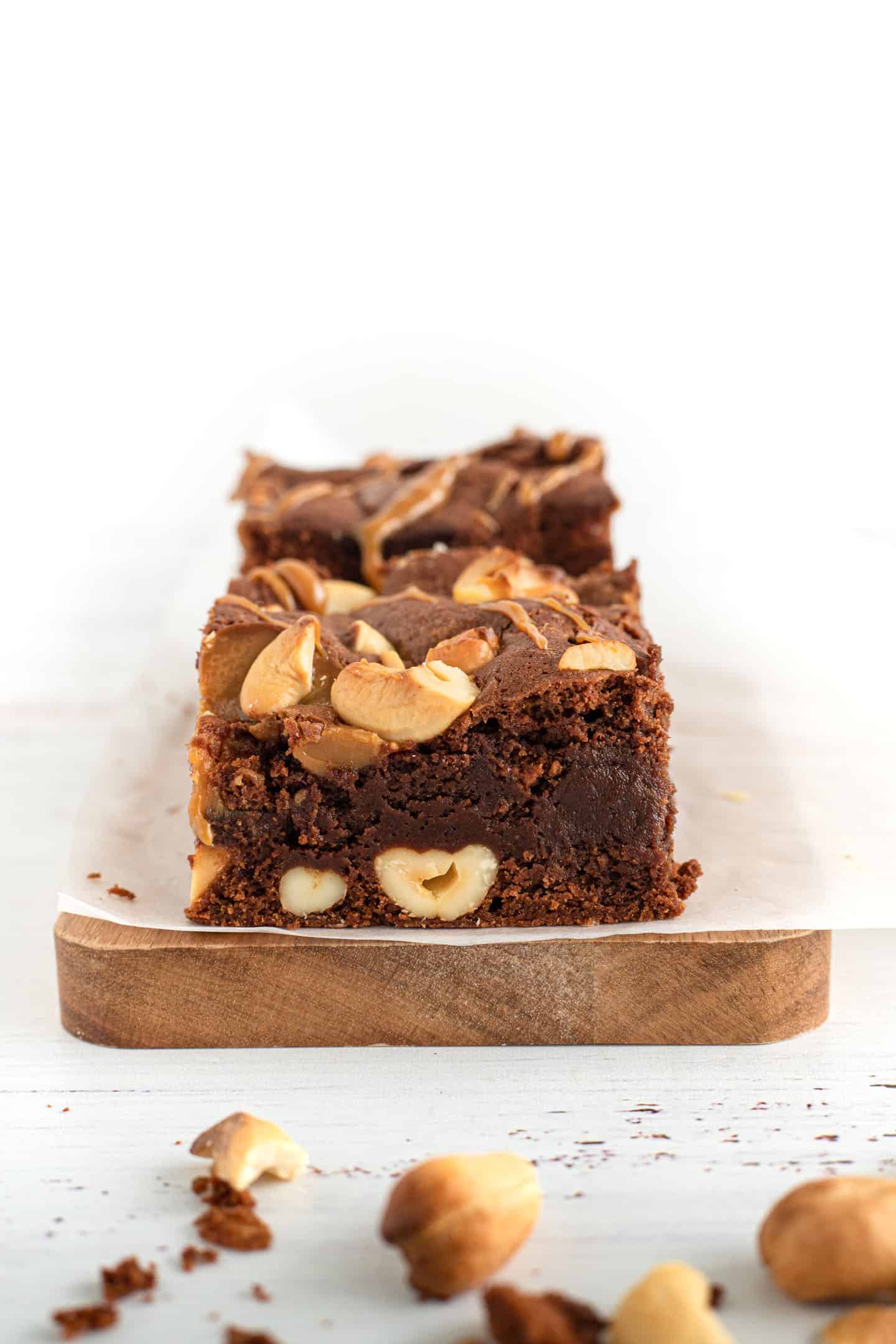 Square of dulce de leche cashews brownie on white parchment paper on a wooden board