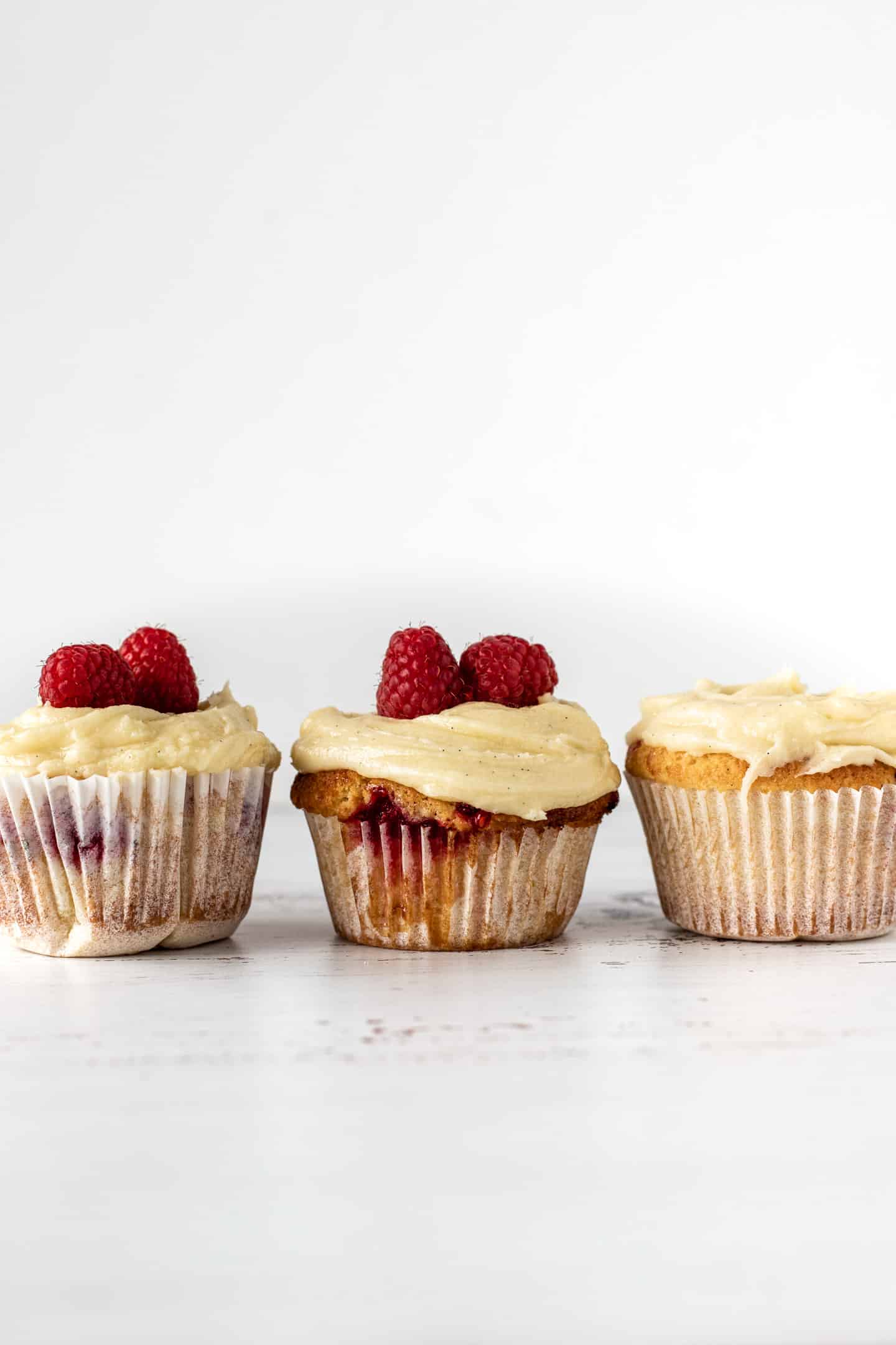 Tres cupcakes, dos con frambuesas sobre la crema de manteca en una superficie blanca y fondo blanco