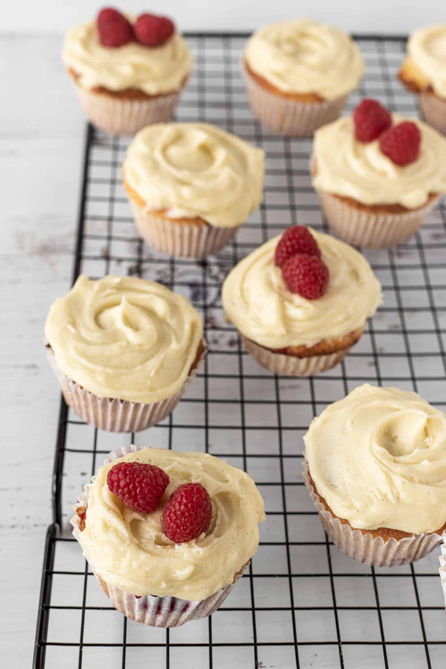 Raspberry and orange cupcakes on a rectangular cooling rack, some with raspberries on top of the buttercream and other without