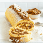 Dulce de leche cake roll on a baking sheet, with a small bowl with dulce de leche behind it