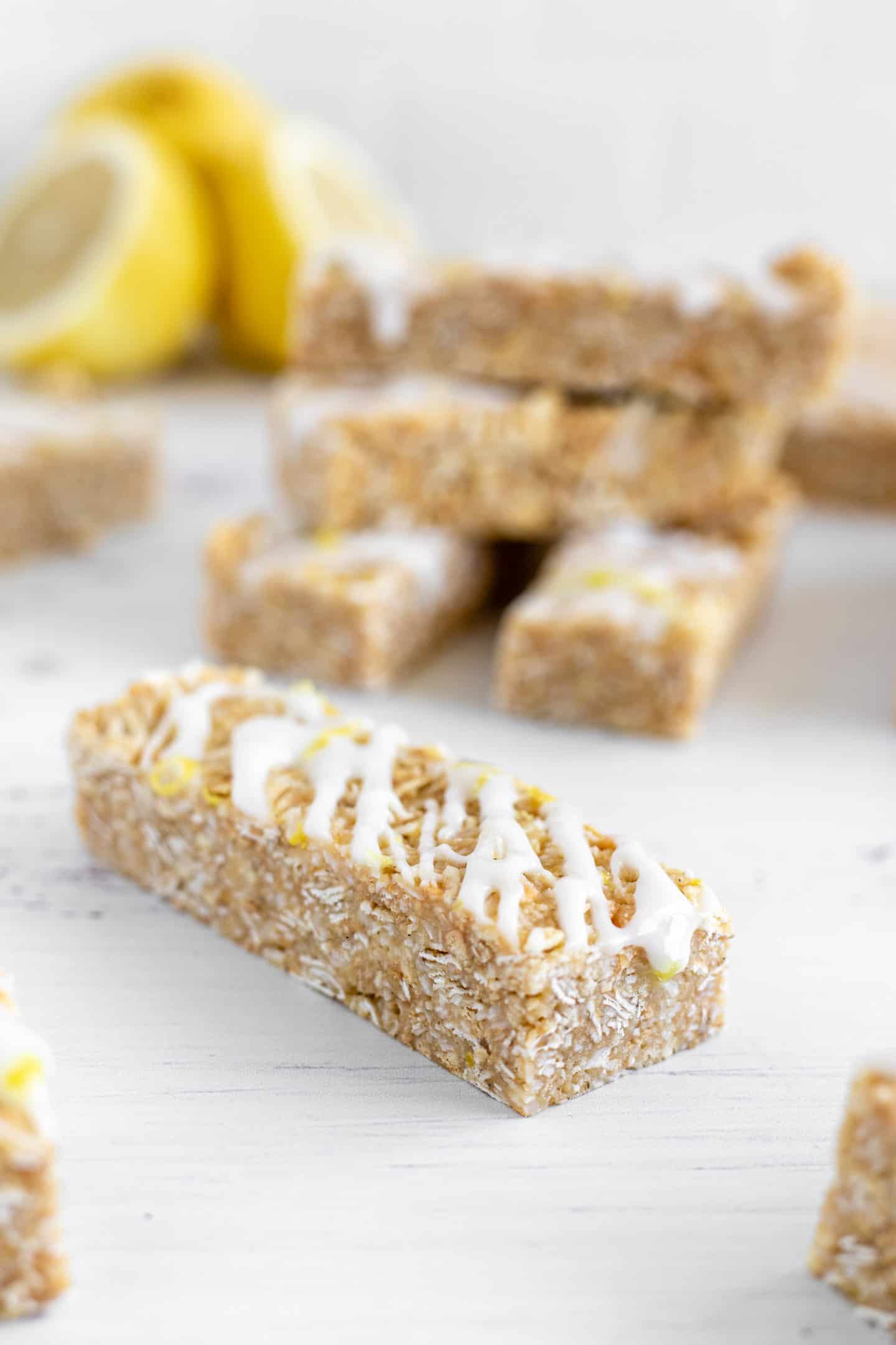 Bars drizzled with some glaze on a white surface and three lemons behind them