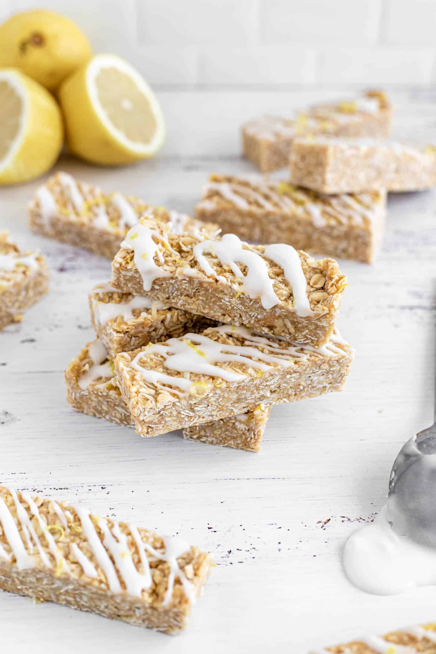 A few bars drizzled with glaze on a white surface, a spoon with some glaze and three lemons at the back