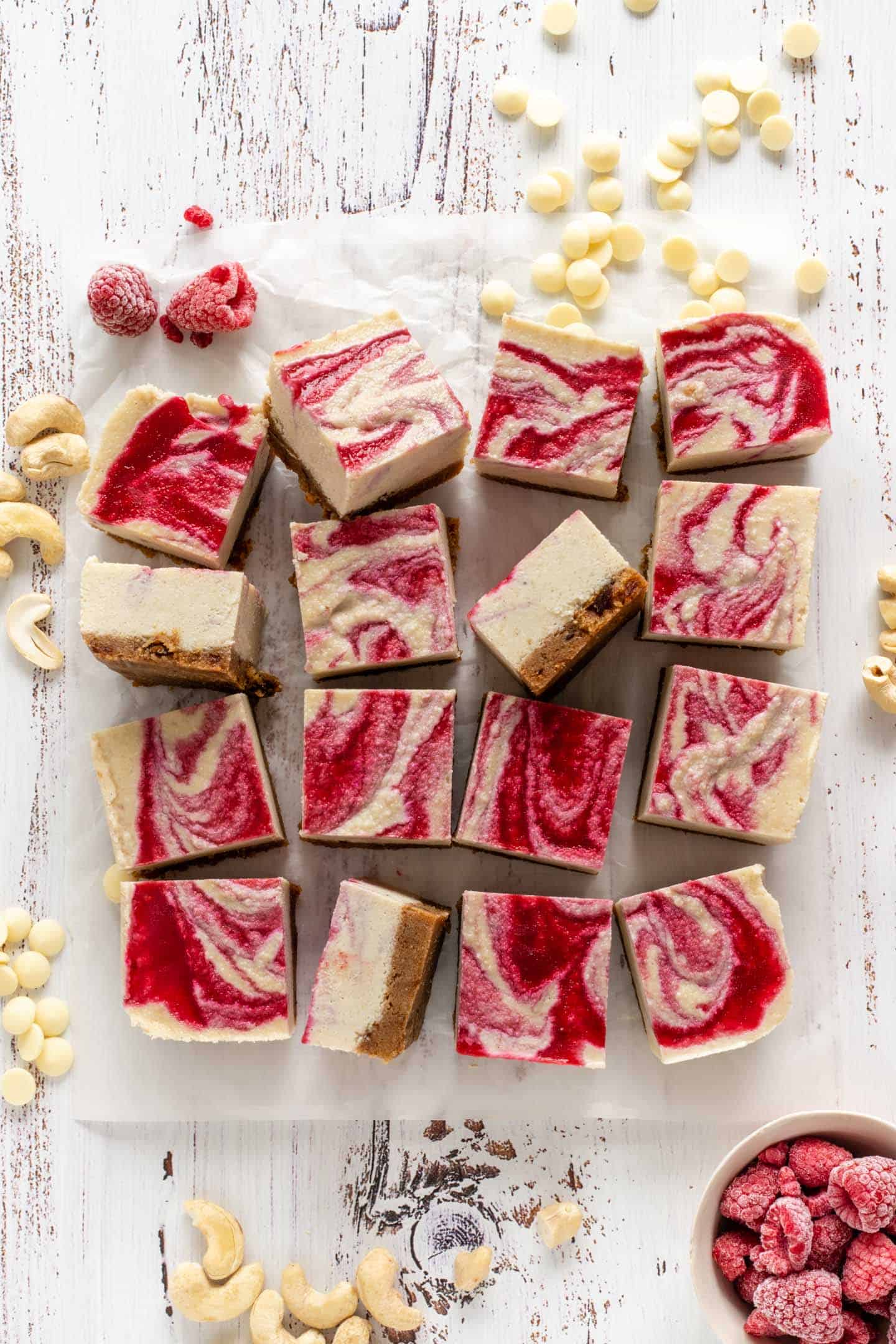 A few frozen bars on some parchment paper, a small bowl with raspberries and small white chocolate chips
