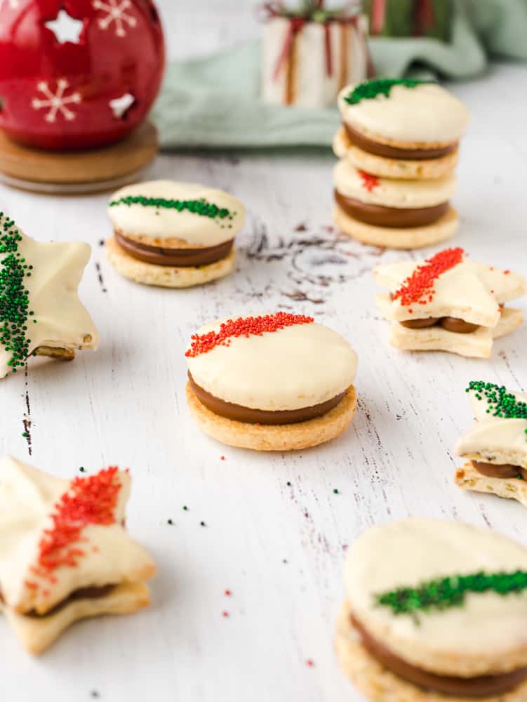 Macadamia alfajores covered in white chocolate and sprinkles on a white surface