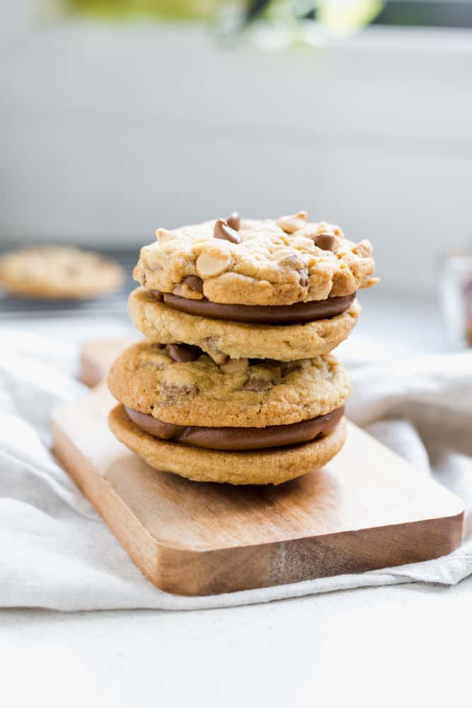 dos alfajores de galletitas con chips de chocolate rellenos de dulce de leche sobre una tabla de madera