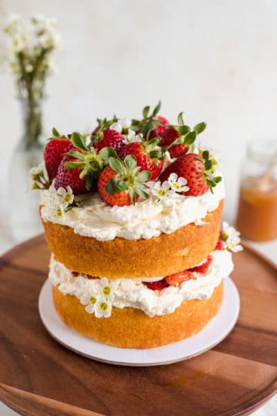 2-layered naked vanilla sponge cake on a wooden cake stand topped with fresh strawberries