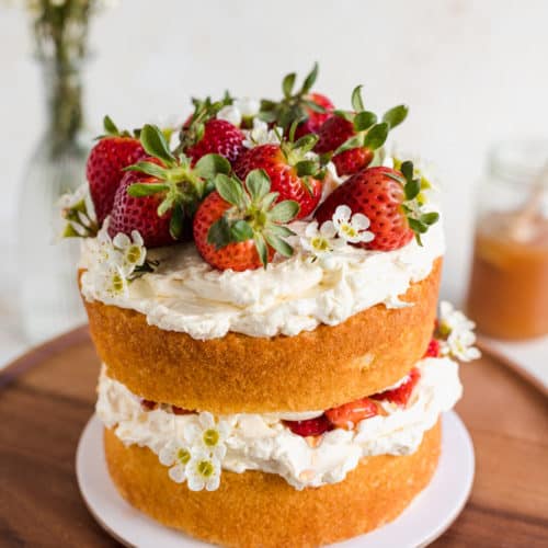 2-layered naked vanilla sponge cake on a wooden cake stand topped with fresh strawberries