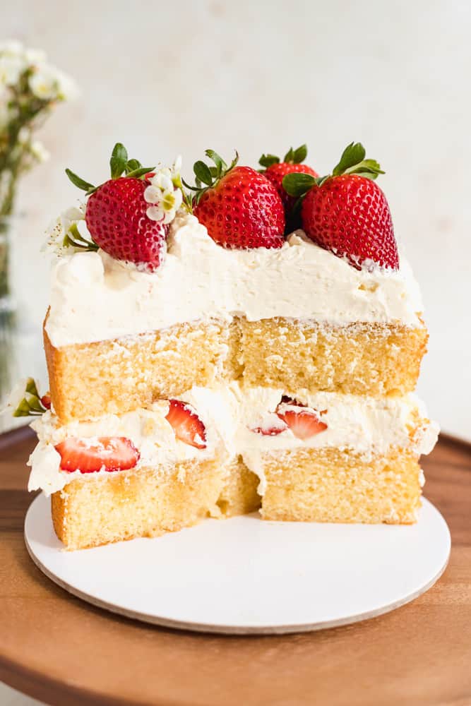 Close up of a two-layered sponge cake, cut in half with fresh strawberries on top