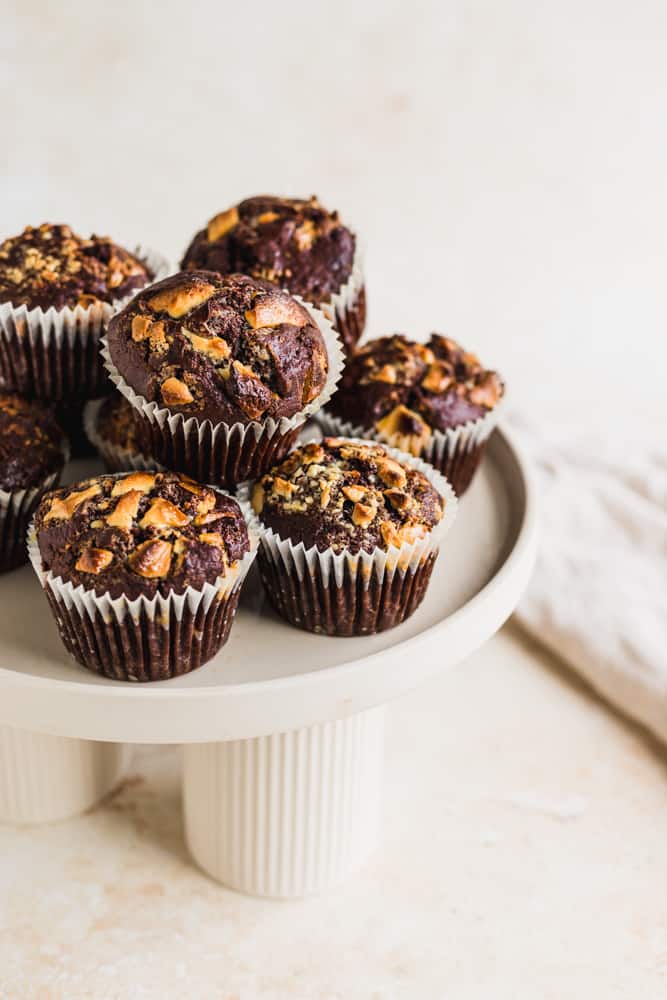 Muffins de banana y doble chocolate sobre una base para tortas blanca y un paño de cocina al fondo