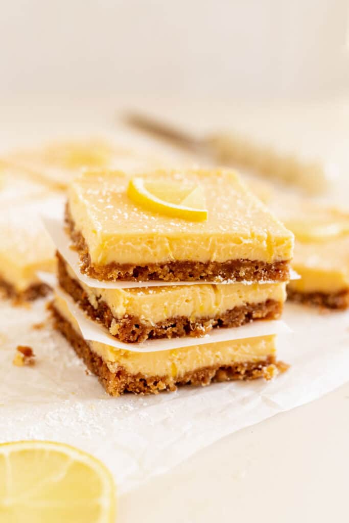 Stack of three lemon bars on some parchment paper and a lemon slice on top